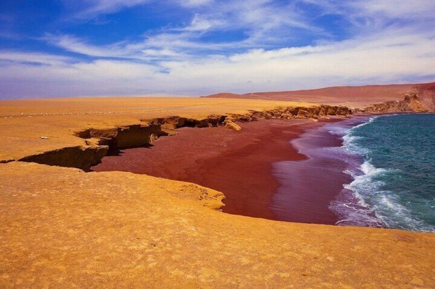 A desert landscape with a red sand beach and a body of water. 1