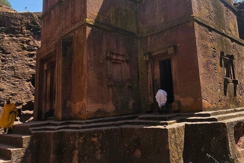 An ancient stone structure with carved doorways and a person in white standing at the entrance. 4