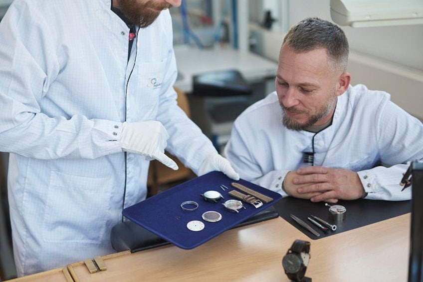 Twee personen in een laboratorium, één wijst naar een schaal met objecten. 2