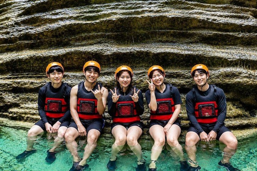 Five people sitting on a rock formation in clear water. 5