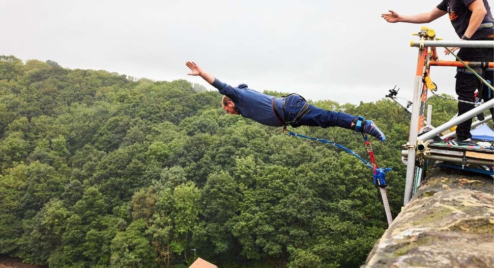 A person bungee jumping off a cliff with a forested landscape in the background. 3