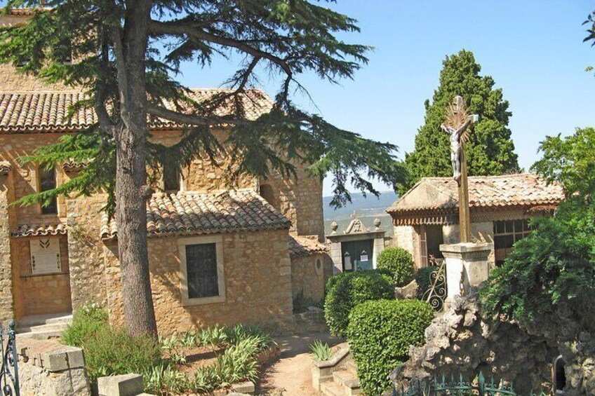 A stone building with a tiled roof, a statue, and a tree in a courtyard. 1