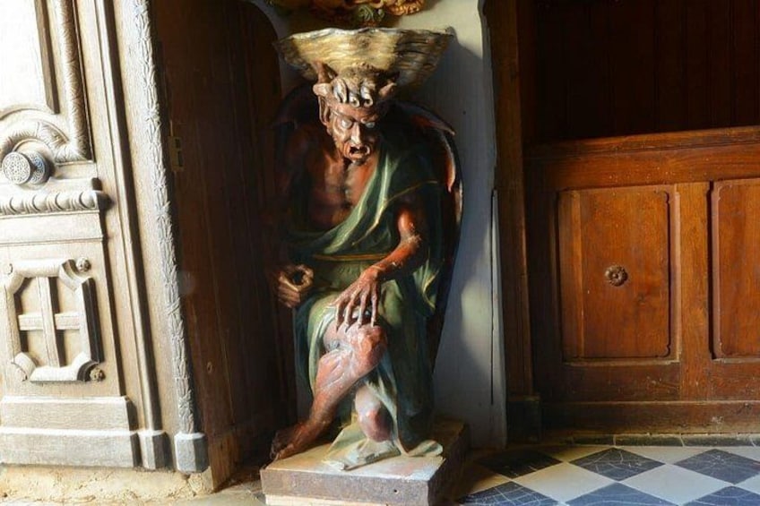 Una estatua de una figura con corona, sentada sobre un pedestal, frente a una puerta de madera con piso de cuadros. 4