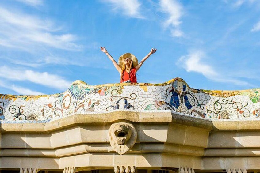 A person standing on a tiled roof with a mosaic design, a stone lion head, and a clear blue sky. 2
