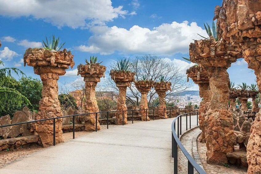 A pathway flanked by stone pillars with vegetation on top, leading towards a mountainous landscape. 5