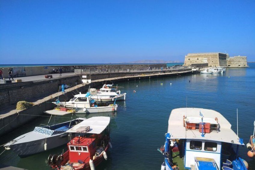 Un puerto con barcos amarrados, un muro de piedra y una fortaleza al fondo. 2