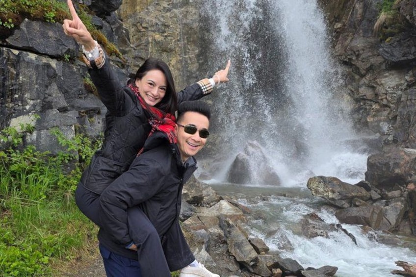 A person carrying another on their back near a waterfall. 3