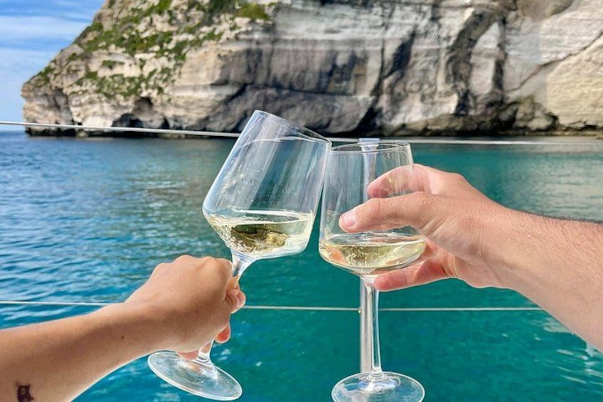 Dos personas brindando con copas de vino frente a un mar azul y acantilados rocosos. 3