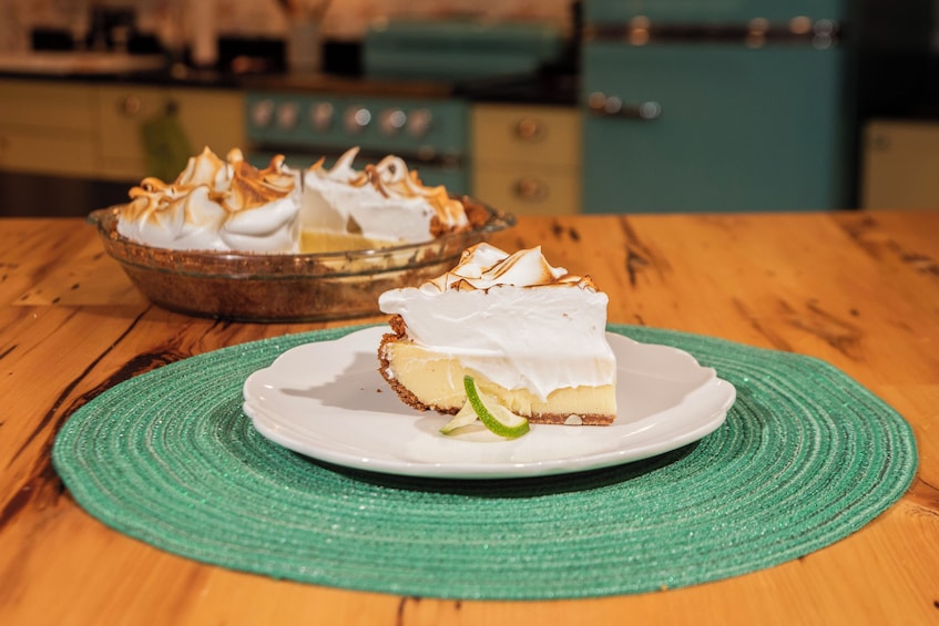 A slice of pie with meringue on a plate, a whole pie in the background, and a green placemat on a wooden table. 2
