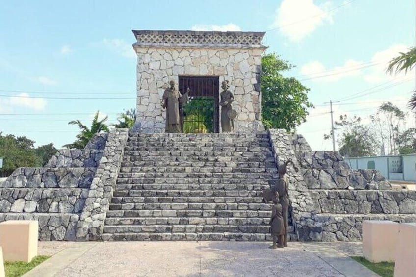 A stone monument with steps leading to a small building, statues, and a clear sky. 1