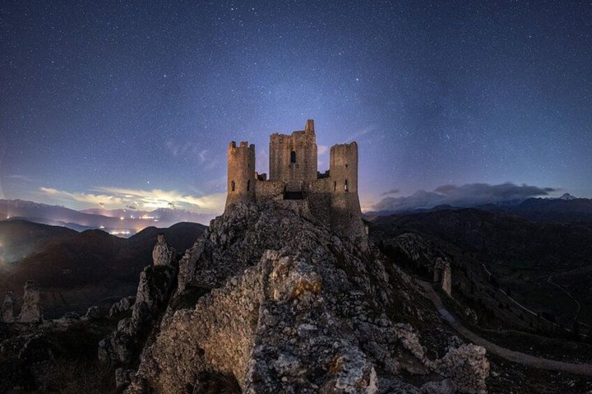 Eine historische Burg auf einem felsigen Hügel unter einem sternenübersäten Nachthimmel. 2