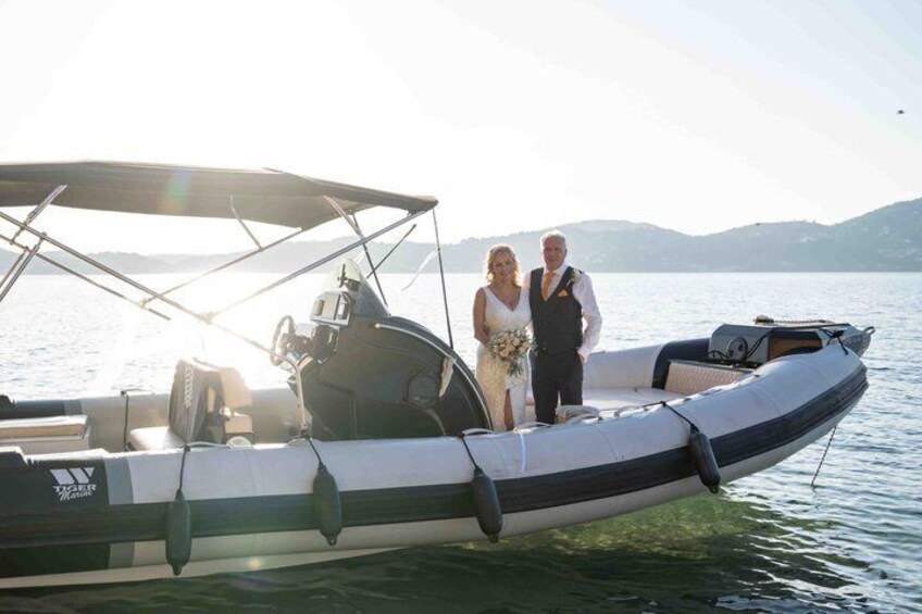 Un couple est à bord d’un petit bateau à moteur, équipé d’un auvent, d’un moteur et d’un volant, sur un lac paisible, avec des montagnes en arrière-plan. 3