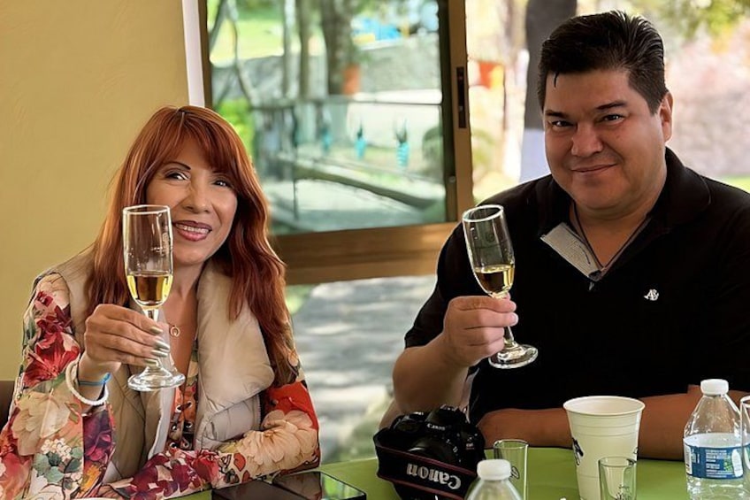 Twee personen zitten aan een tafel met drankjes, een camera en een waterfles. 2
