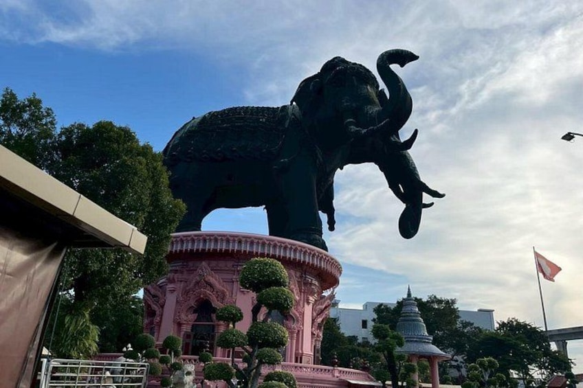 En stor elefantstaty på en rosa piedestal, med ett pagodliknande tempel i bakgrunden. 3