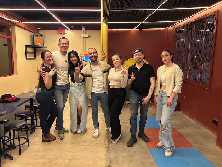 A group of people posing indoors with a red wall and a yellow circular decoration in the background. 2