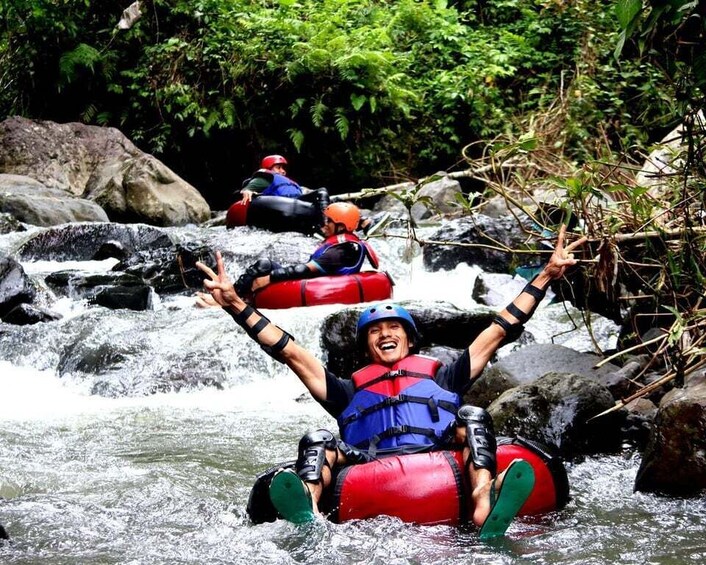 Two people rafting down a river surrounded by rocks and greenery. 1