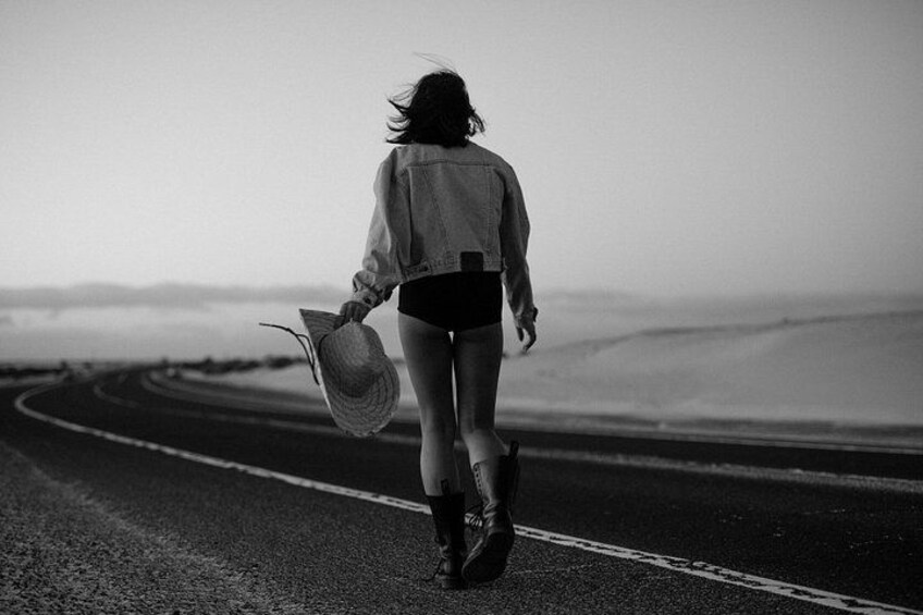 A person walking on a road with a hat, holding a bag, and wearing boots. 4