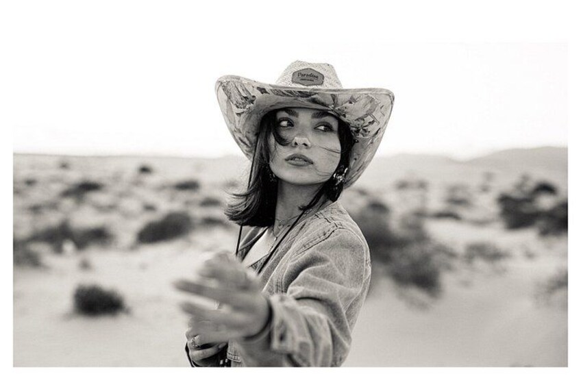 A person in a wide-brimmed hat and a long-sleeved shirt standing in a desert landscape. 5