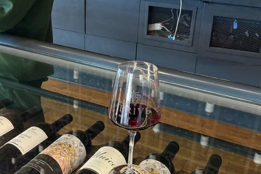 A wine glass with red wine on a counter with wine bottles. 3