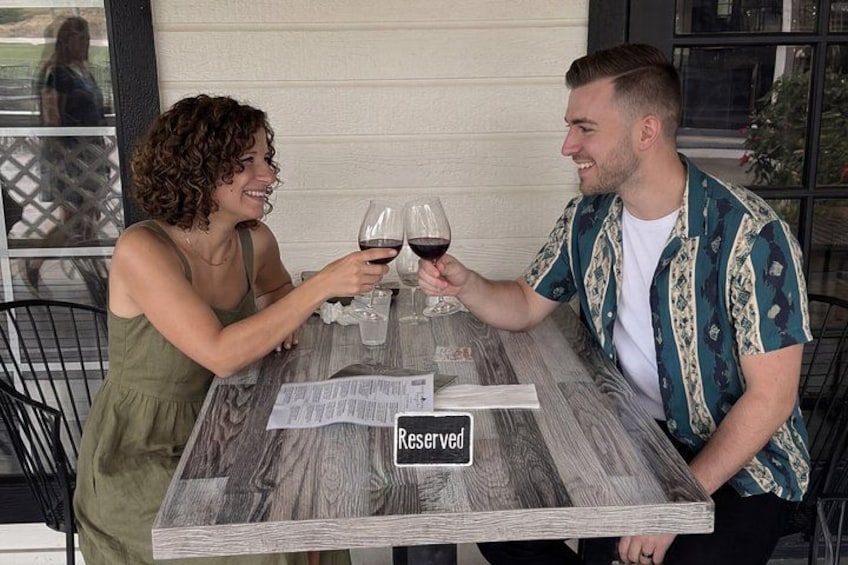 Two people sitting at a table with a 'Reserved' sign, holding wine glasses. 5