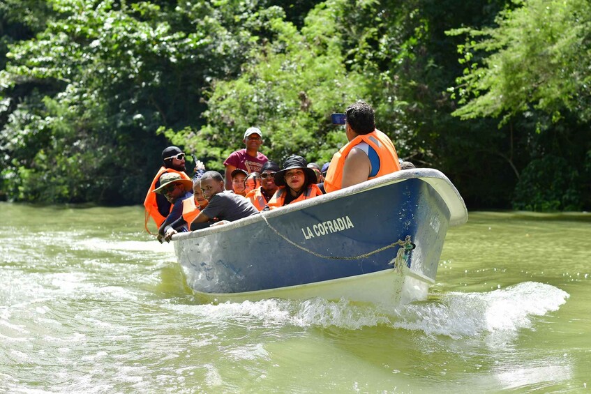 A boat named 'LA COFRADIA' with passengers wearing orange life jackets on a river surrounded by greenery. 5