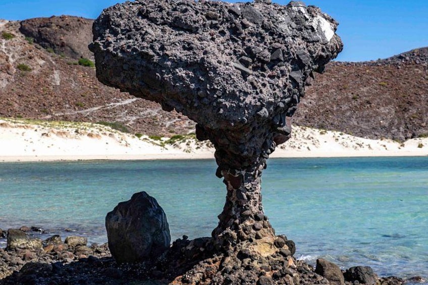 En unik klippformation med en platt topp och en bred bas, omgiven av kristallklart blått vatten och en sandstrand. 2