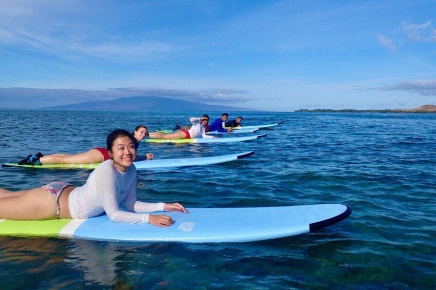 People lying on surfboards in the water, with a clear sky and distant land in the background. 1