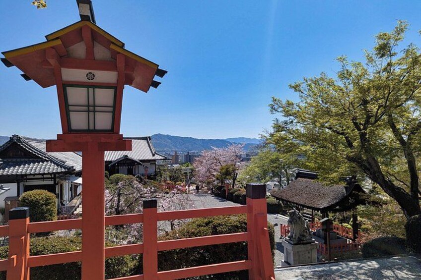 A traditional Japanese gate with a lantern, cherry blossoms, and a mountain range in the background. 1