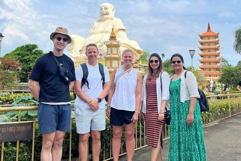 A group of people standing in front of a large golden statue and a pagoda. 4