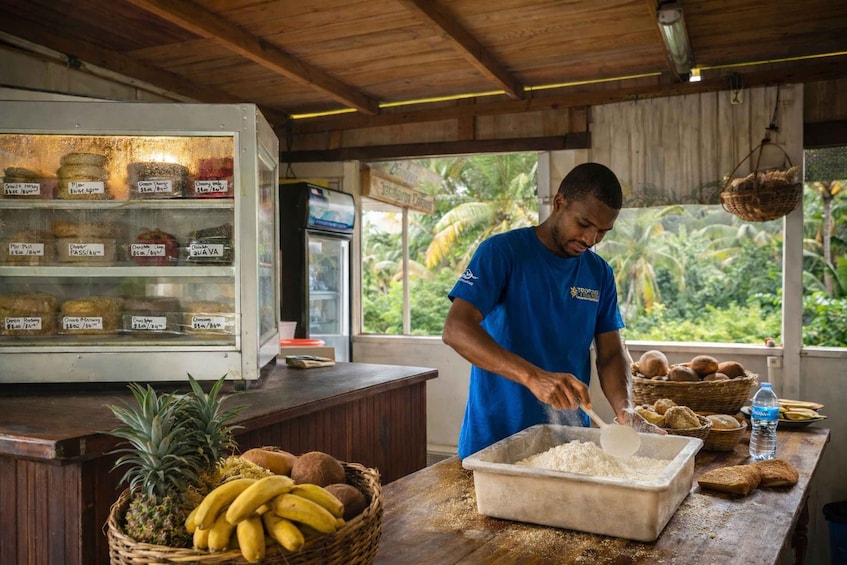 A person in a blue shirt preparing food at a wooden counter with a display case of preserved foods and a tropical view. 5