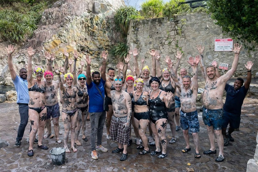 A group of people covered in mud, standing in a rocky outdoor area with a sign that reads 'NOTICE.' 1