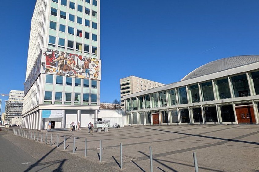 Un bâtiment moderne orné d’une fresque murale, doté d’une grande entrée en verre et surplombant un ciel d’un bleu éclatant. 4