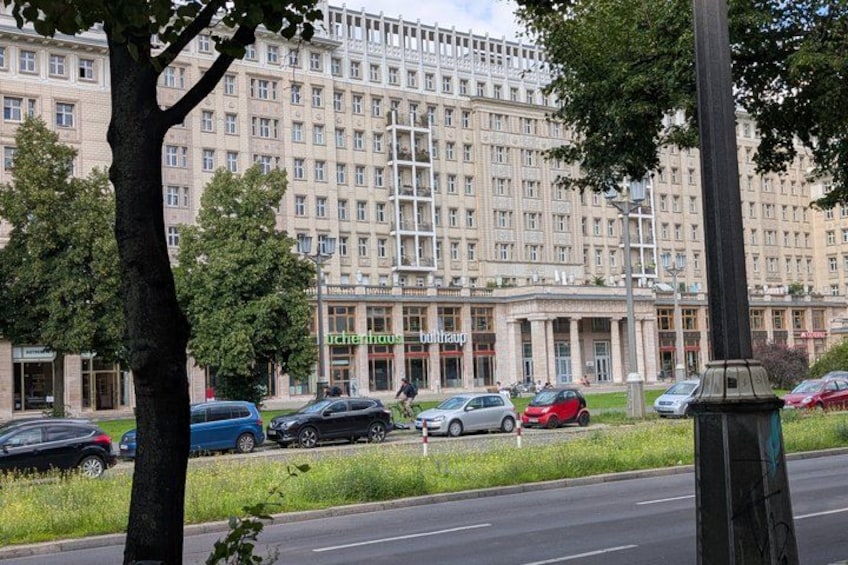 Ein großes Gebäude mit vielen Fenstern, eine Straße mit Autos und ein Baum im Vordergrund. 4