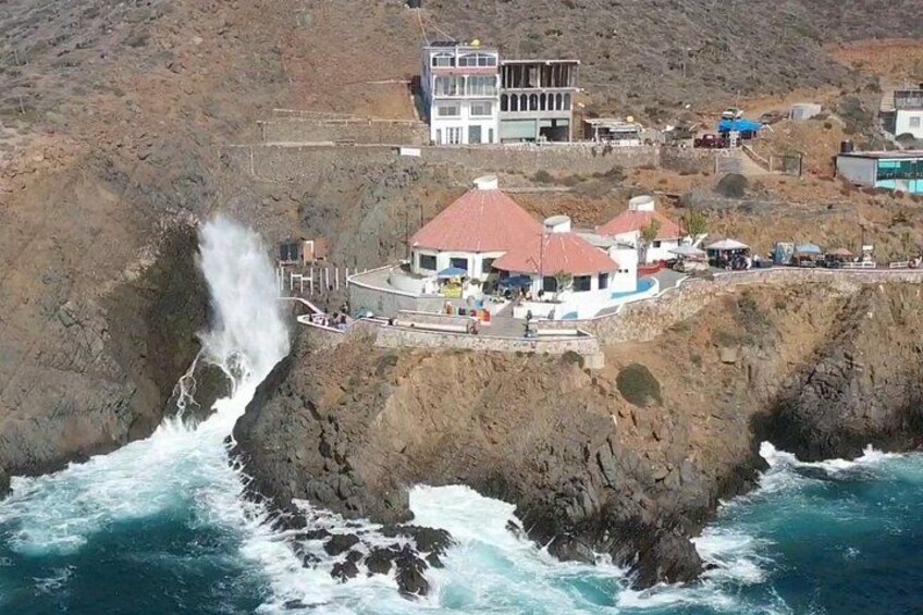 Un bâtiment situé sur la côte, avec un toit rouge, une falaise rocheuse et des vagues qui s’écrasent contre les rochers. 3