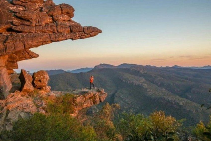 A person standing on a rocky outcrop with a view of a mountainous landscape. 2