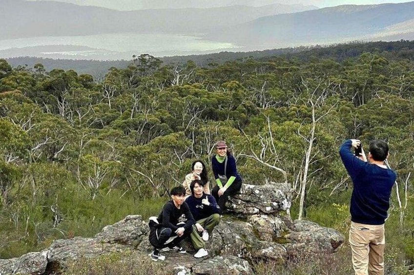 A group of people sitting on rocks with a forest and mountains in the background. 1