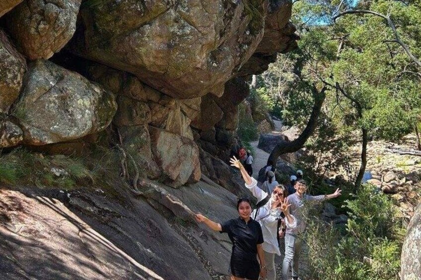 A group of people standing on a rocky path with trees and a large rock formation in the background. 5