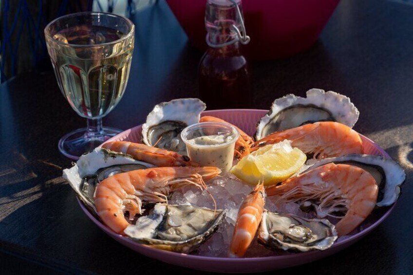 A plate of seafood including shrimp and oysters, a lemon wedge, and a glass of white wine on a table. 4