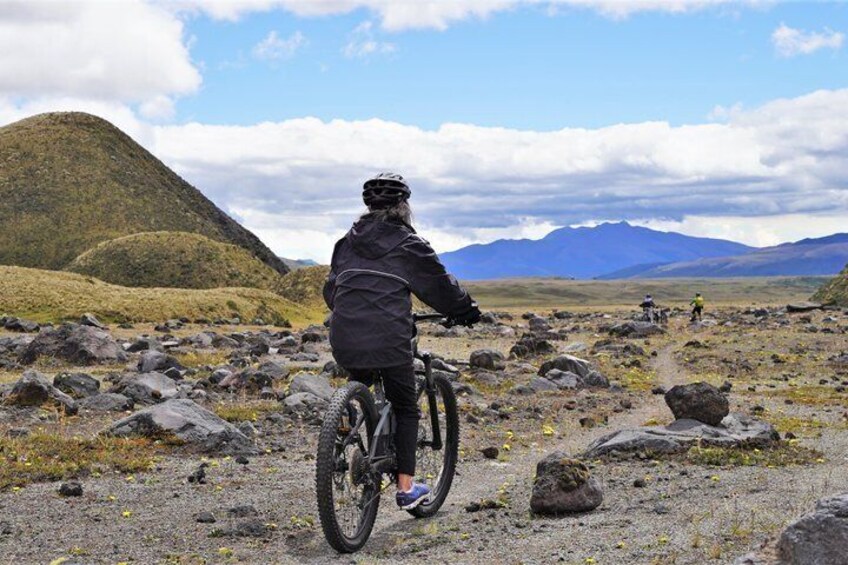 En person cykler på en mountainbike på en stenet sti med bjerge i baggrunden. 2