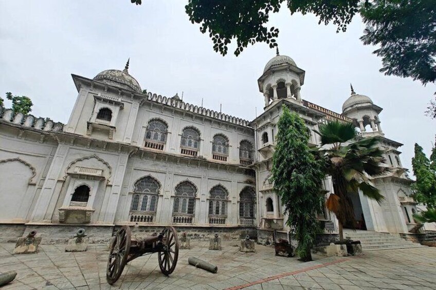 A large white building with domes and arched windows, surrounded by trees and a cart. 4