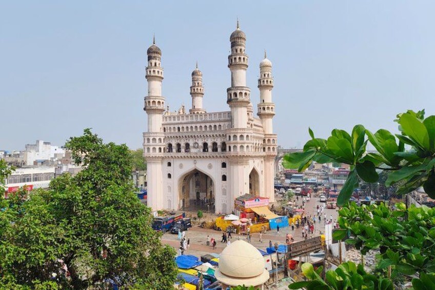 Een groot, sierlijk gebouw met meerdere minaretten, omgeven door een levendig marktgebied met kleurrijke parasols en mensen. 5
