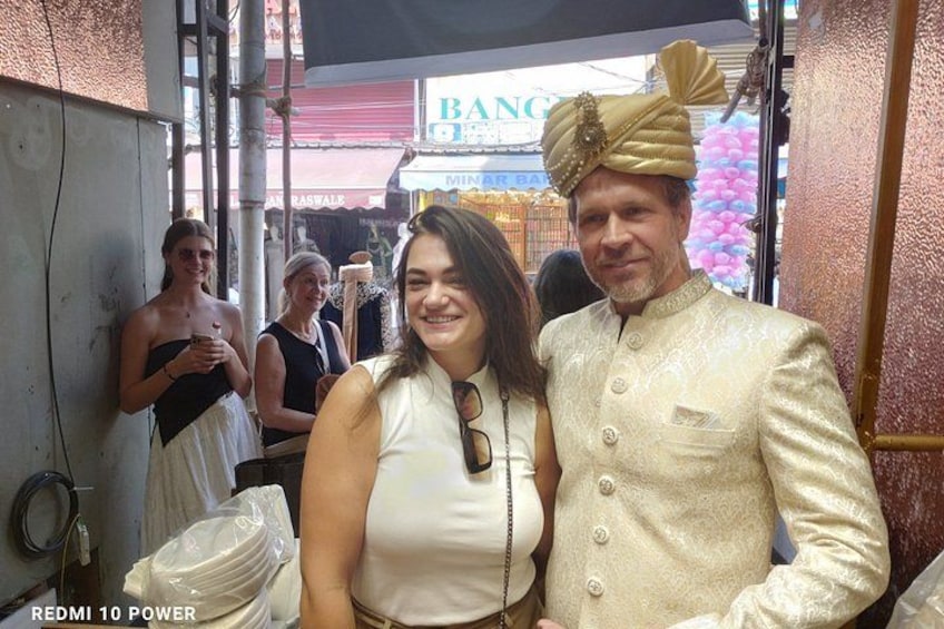 A man in a traditional outfit with a turban, a woman in a white dress, and a background with a sign that reads 'BANK'. 4