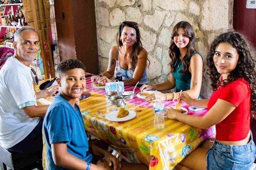 A group of people sitting around a table with a colorful tablecloth, engaged in conversation. 1
