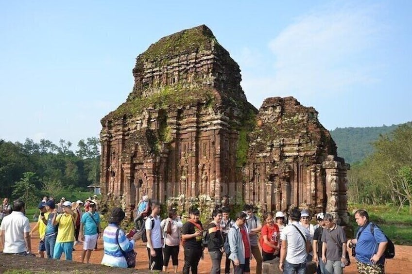 Een groep toeristen staat voor een eeuwenoud tempel met ingewikkelde gravures en een grote, terrasvormige constructie. 4