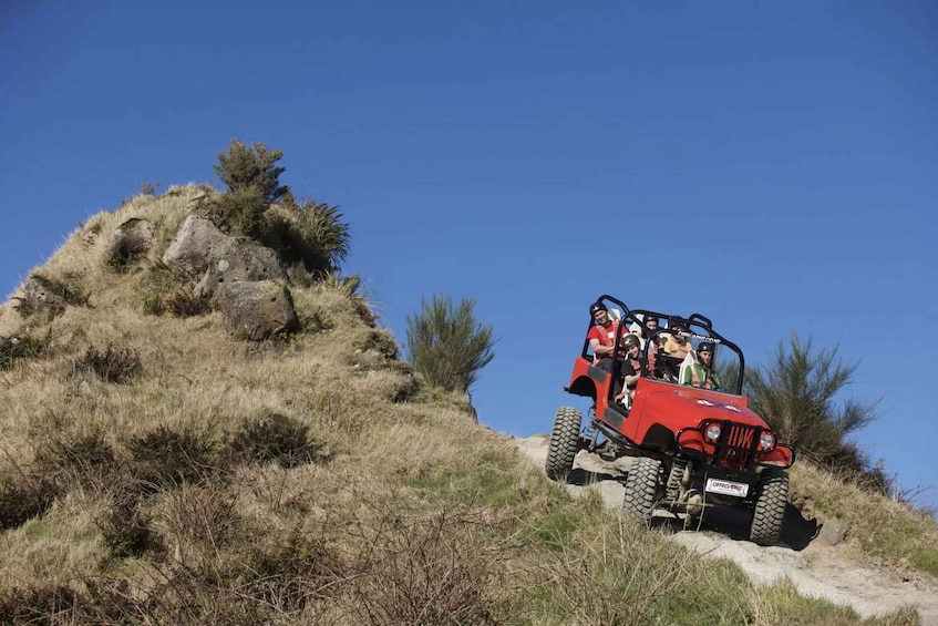 A red off-road vehicle on a dirt path with passengers, surrounded by dry grass and sparse vegetation. 3