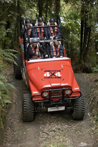 A red off-road vehicle with 'Monster 4x4 Thrill Ride' and 'OffroadNZ' branding, driven by a person, on a forest trail. 1
