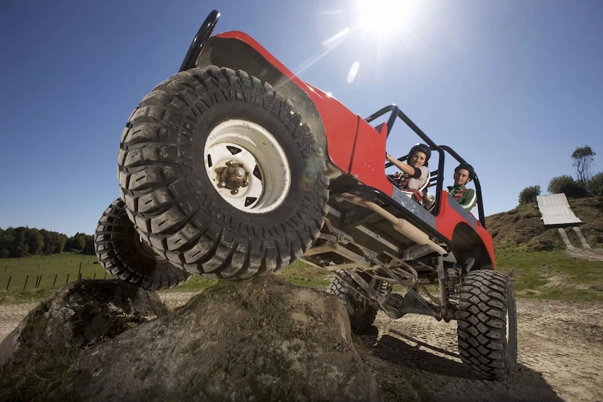 A red off-road vehicle on a dirt path with a large rock in the foreground. 2