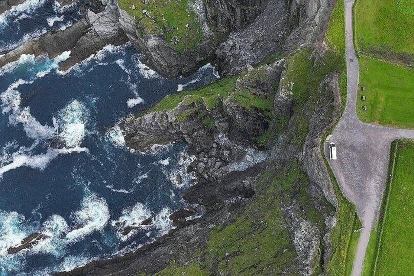 Paisaje costero con acantilados rocosos, olas rompiendo contra la orilla y una carretera serpenteando a lo largo de la costa. 3