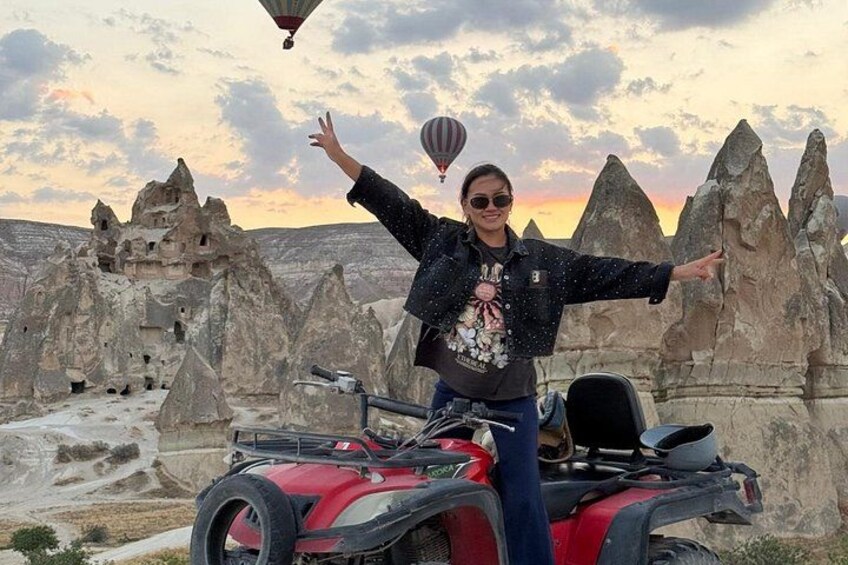 Una persona parada en un cuatrimoto rojo, con un paisaje desértico que incluye formaciones rocosas al fondo. 2