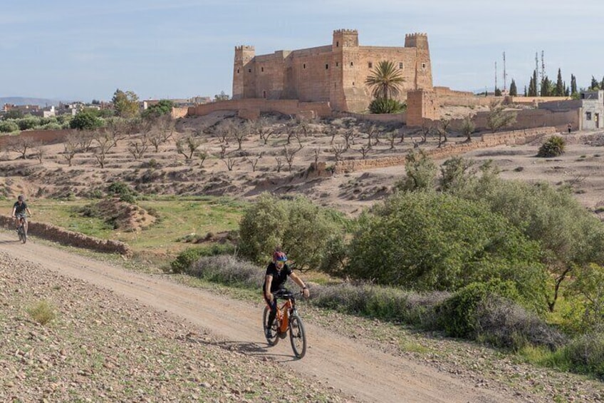 Un cycliste sur un chemin de terre, avec un château historique en arrière-plan. 1